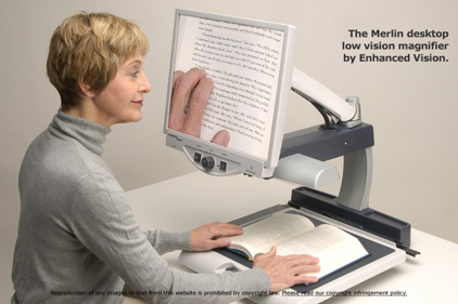 The Merlin desktop magnifier being used to magnify book text. A white woman in her mid 60's is reading the text from the book off of the magnifier's screen.